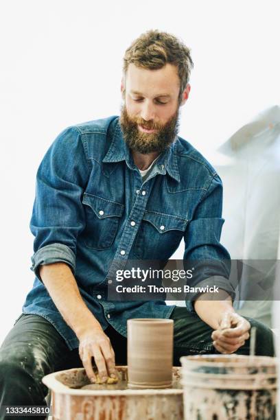 medium shot of male pottery artist cleaning potters wheel after working on project in studio - rolling up sleeve stock-fotos und bilder