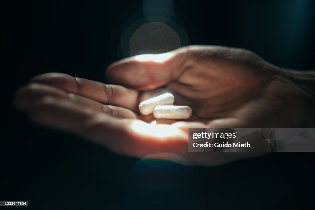 Hand holding 2 pills in sunlight.