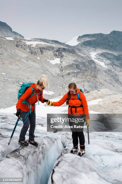 female mountain climber lends a hand to another women who is crossing a crevasse - crevasse fotografías e imágenes de stock