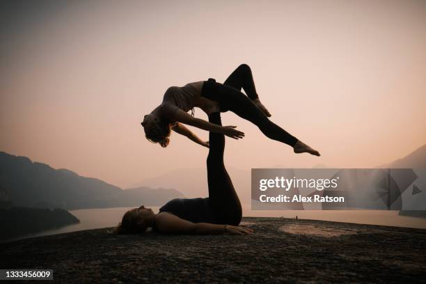 silhouette of two people performing acro yoga at sunset - acroyoga stock pictures, royalty-free photos & images