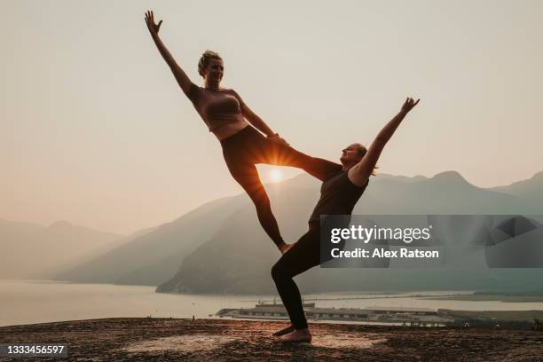 two women do acroyoga on top of cliff during dramatic sunset - acroyoga stock pictures, royalty-free photos & images