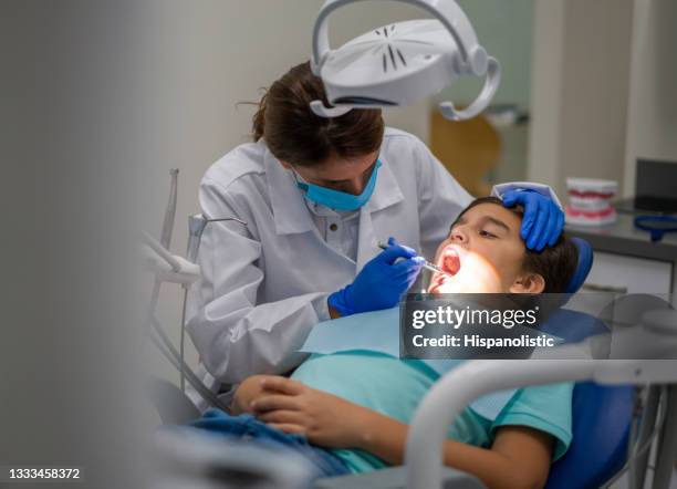 dentista limpiando los dientes de un niño durante una consulta - odontopediatría fotografías e imágenes de stock