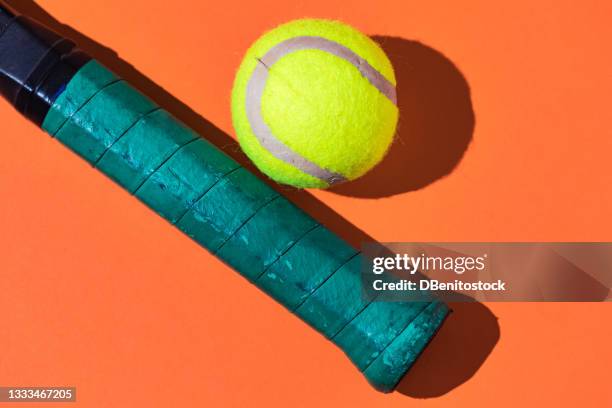 yellow tennis ball next to green tennis racket grip on orange background - tennis racquet isolated stock pictures, royalty-free photos & images