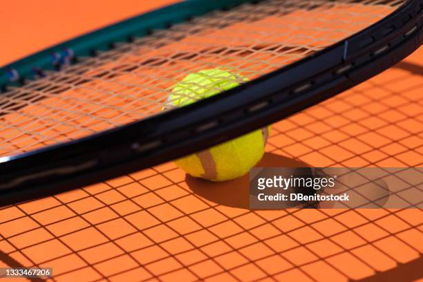 yellow tennis ball with focused hard shadow, under the string of a racket on orange background - abstract tennis player stock pictures, royalty-free photos & images