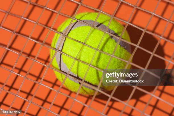 yellow tennis ball with hard shadow under the string of a racket on orange background - abstract tennis player stock pictures, royalty-free photos & images