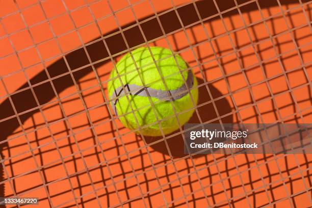 yellow tennis ball with hard shadow on the strings of a racket on orange background - abstract tennis player stock pictures, royalty-free photos & images