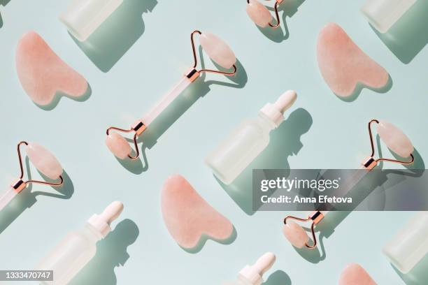 rose quartz roller and guasha near white matte glass bottle with face serum on pastel light blue teal background. massagers are used for anti aging procedures with an oil or moisturizer. pattern - spooning stock pictures, royalty-free photos & images