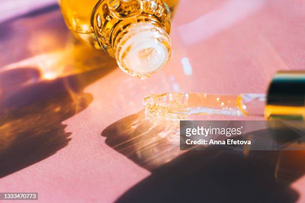 glass bottle and pipette with bright yellow essential oil placed on pastel pink background. play of shadow and light creates an abstract pattern. concept of organic body care cosmetic. trendy colors of the year 2021. extreme close-up - argan oil stock-fotos und bilder
