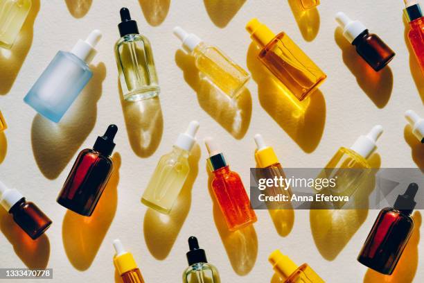 set of many different glass bottles with cosmetic liquids on white surface. play of light creates abstract patterns from shadows and illuminating yellow reflections. trendy colors of the year 2021. flat lay style - cosmetica fotografías e imágenes de stock