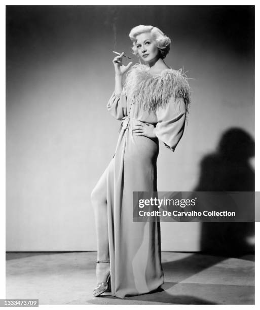 Actress Marilyn Maxwell wears a robe and smokes while holding a cigarette case as 'Charlotte Maynard' in a publicity shot from the movie 'Outside the...
