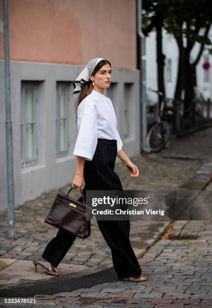 Guest is seen wearing black striped pants, white button shirt, head scarf outside Lovechild on August 10, 2021 in Copenhagen, Denmark.