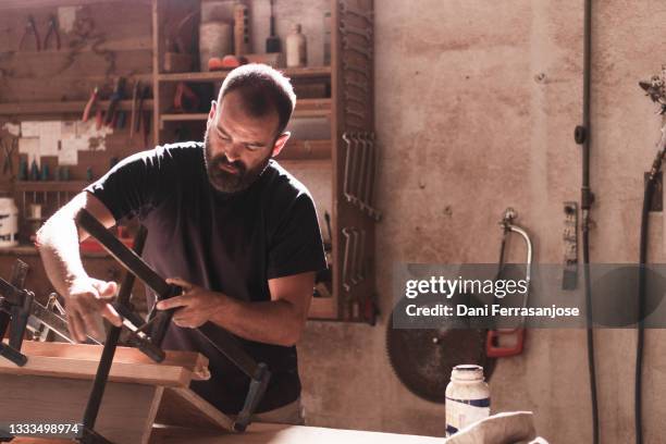 young carpenter working in the workshop using jacks to make a piece of furniture - hispanic construction worker stock-fotos und bilder