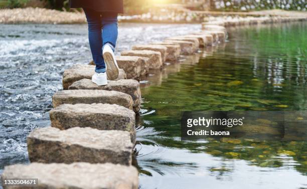 donna che attraversa un fiume su pietre miliari - trail foto e immagini stock