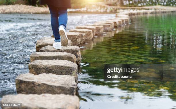 woman crossing a river on stepping stones - de volgende stap stockfoto's en -beelden