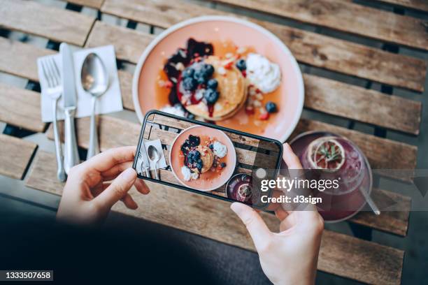 overhead view of young asian woman taking photos of delicious freshly served pancakes with blueberries and pink lemonade with smartphone before eating it in cafe. eating out lifestyle. camera eats first culture - iphone camera stock pictures, royalty-free photos & images