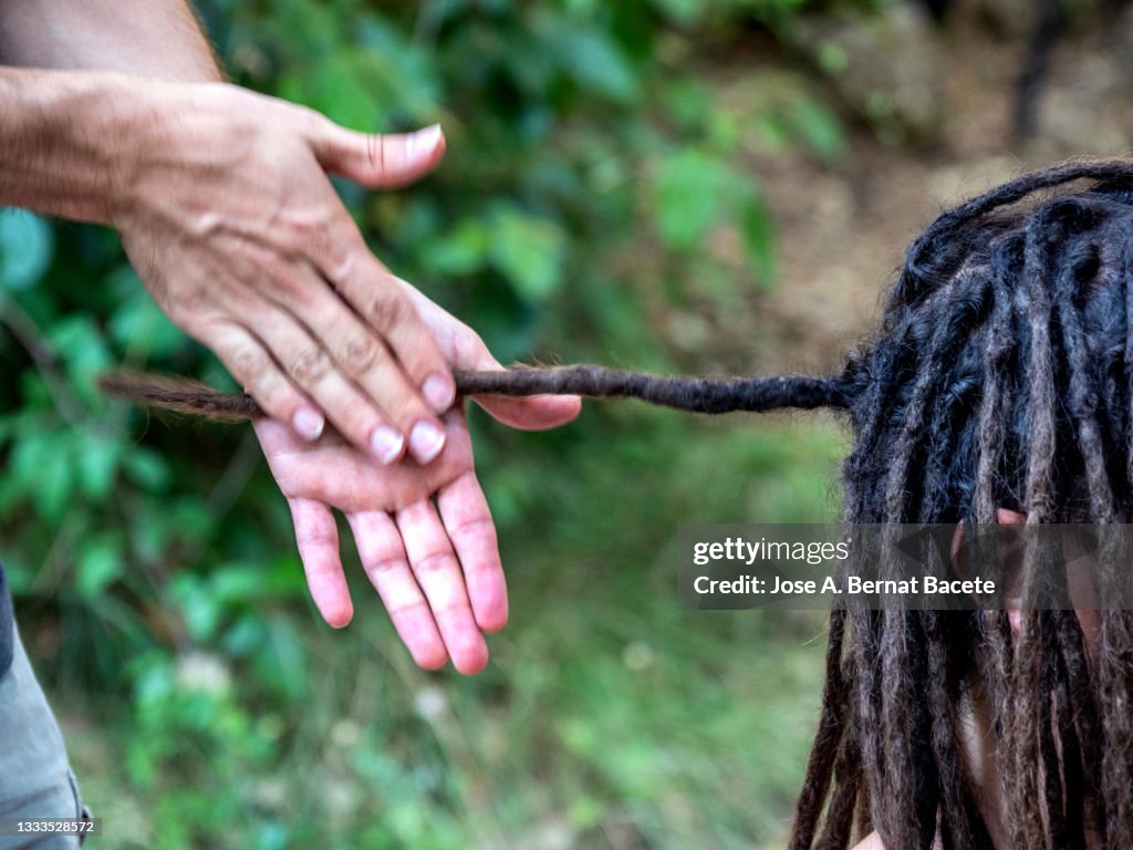 Man with dreadlocks, he styles his hair with a hairdresser outdoors in nature.
