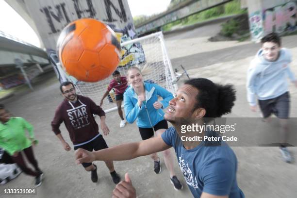 group of young adults playing football in city - street football stock-fotos und bilder