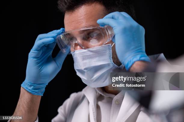 männlicher wissenschaftler, der vor einem experiment schutzbrillen anschnauft - get dressed male stock-fotos und bilder