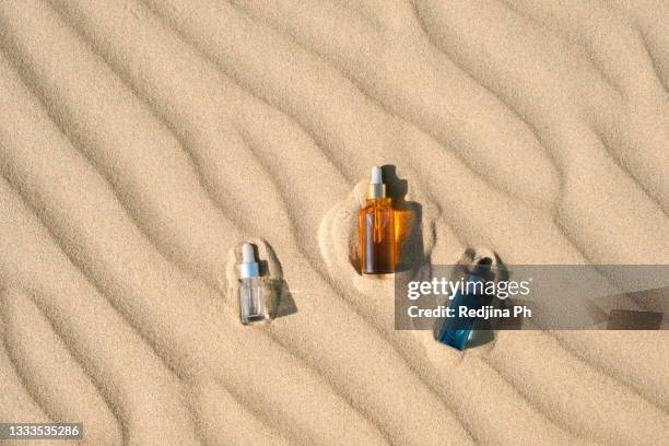 three bottles of sunburn oil or serum, moisturizer, sunscreen on sand background with hard shadow. top view. flat lay. - areia - fotografias e filmes do acervo