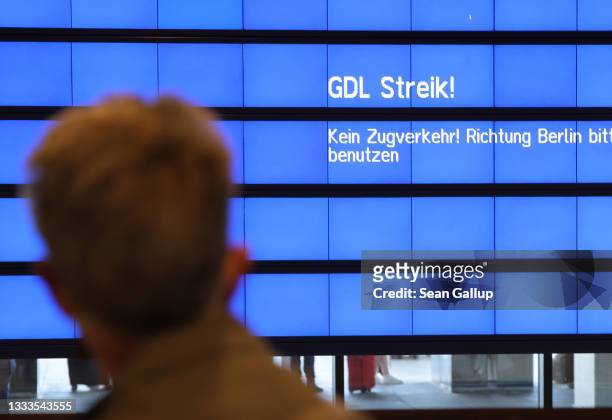 Woman at Berlin Brandenburg Airport walks past a train departures screen warning of a strike by the GDL labor union during a nationwide railway...
