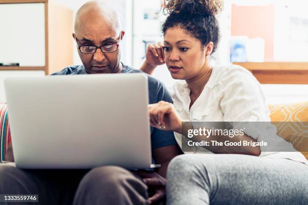 couple looking at laptop while sitting on sofa at home - 40s laptop stock-fotos und bilder