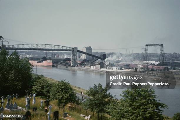 Coal conveyor belt bridge crosses the River Ribble with a cargo vessel moored at the dock area on the north bank of the river in the City of Preston,...