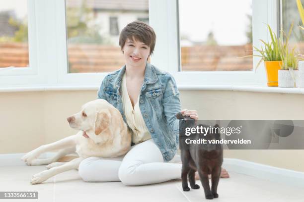young lady in her conservatory with her dog and cat - cat with cream stockfoto's en -beelden