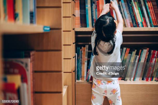 little asian girl choosing books from the bookshelf in library - kinderbuch stock-fotos und bilder