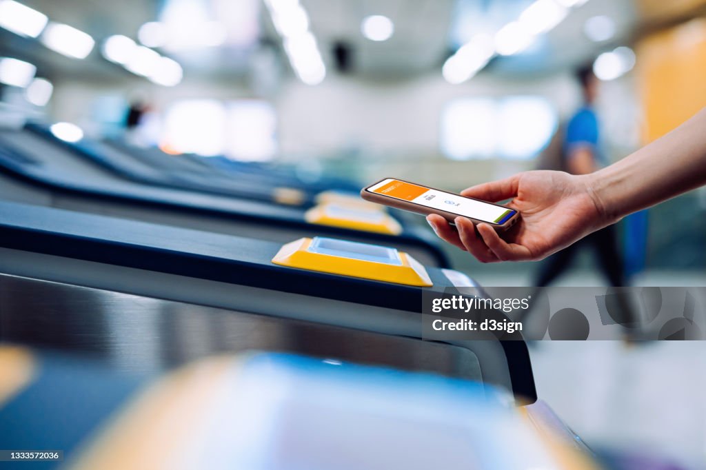 Cropped shot of young Asian woman checking in at subway station, making a quick and easy contactless payment for subway ticket via smartphone. NFC technology, tap and go concept