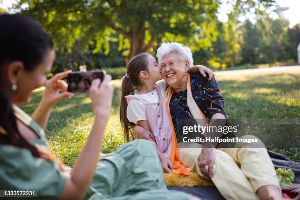 small girl with mother and grandmother resting in a park, taking photographs. - grandparents stock pictures, royalty-free photos & images