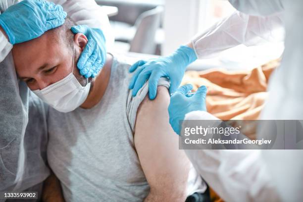 scared balding male getting calmed down by medical workers while taking covid-19 vaccine - epidemic stock pictures, royalty-free photos & images