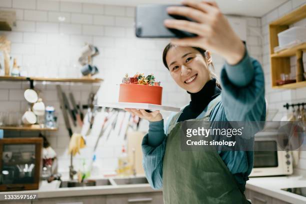 asian female chef posing with her cake in the kitchen - woman making cake stock-fotos und bilder
