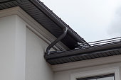 Corner of house with new gray metal tile roof and rain gutter. Metallic Guttering System, Guttering and Drainage Pipe Exterior