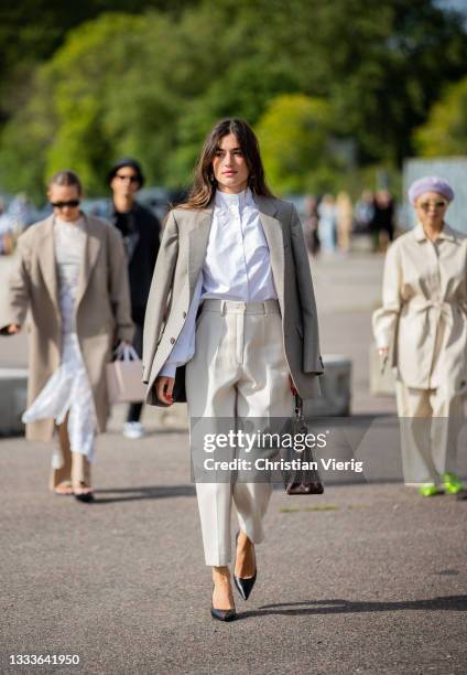 Guest is seen wearing creme white pants, button shirt, grey blazer, bag outside Samsøe Samsøe on August 11, 2021 in Copenhagen, Denmark.