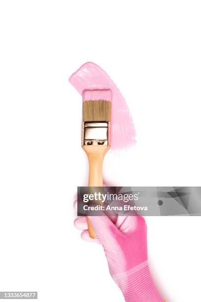 hand in rose protective glove holds paintbrush above metal jar with pink pigment against pastel pink background. concept of home repair. flat lay style - pastel colored stock-fotos und bilder