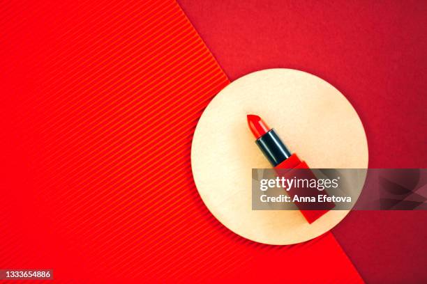 open bright red lipstick is lying on circle shape podium on background made of corrugated and common red paper. flat lay style with copy space - podium mode stock-fotos und bilder