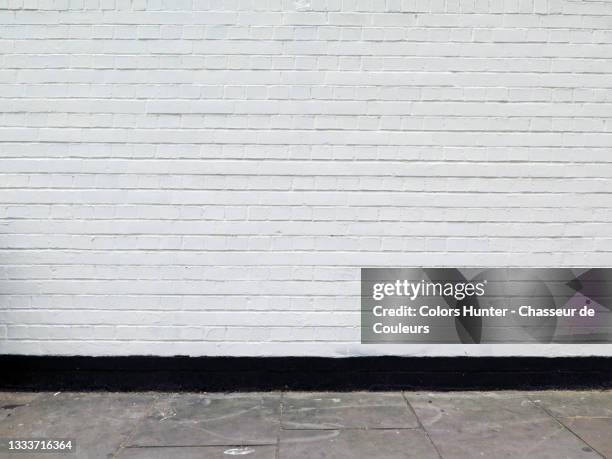 painted brick wall and weathered sidewalk in london - brick wall stockfoto's en -beelden