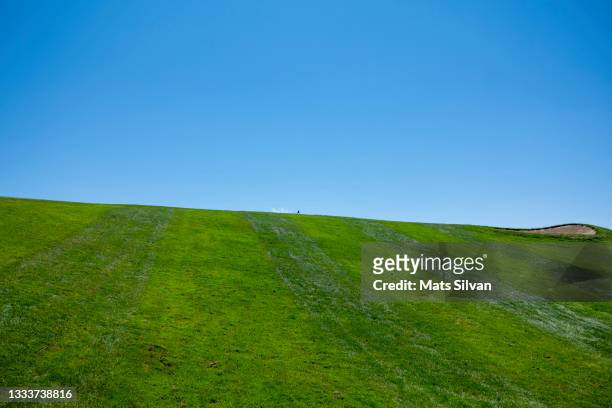 green fairway against blue clear sky with golf flag and sand trap - golf bunker low angle stock pictures, royalty-free photos & images