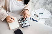 woman writing a list of debt on notebook calculating her expenses with calculator