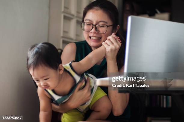 a young southeast asian woman distracted with his son while working at home with laptop on the desk - daily life in philippines stockfoto's en -beelden