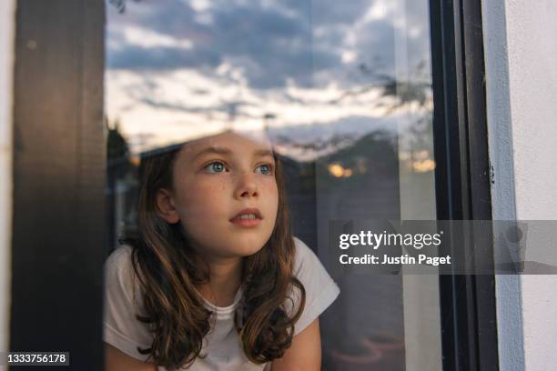 young girl looking out of her window at sunset - girl looking through window stock pictures, royalty-free photos & images