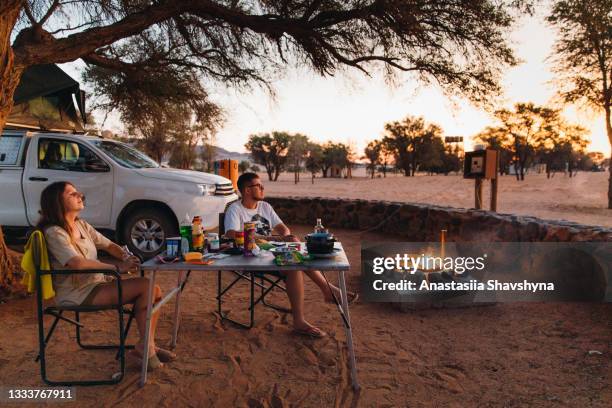 woman and man traveler camping with a camper car under the tree during sunset in the desert of namibia - kalahari desert stockfoto's en -beelden