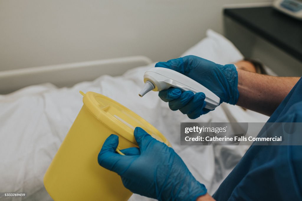 A medical practitioner disposes of a plastic cap on a infrared ear thermometer