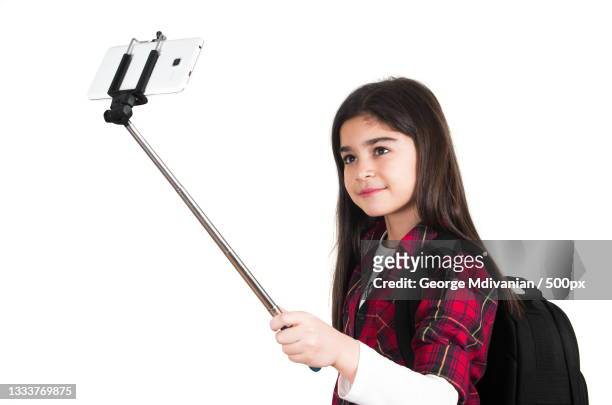 portrait of girl taking selfie standing against white background with selfie stick - selfie stick white background stock-fotos und bilder