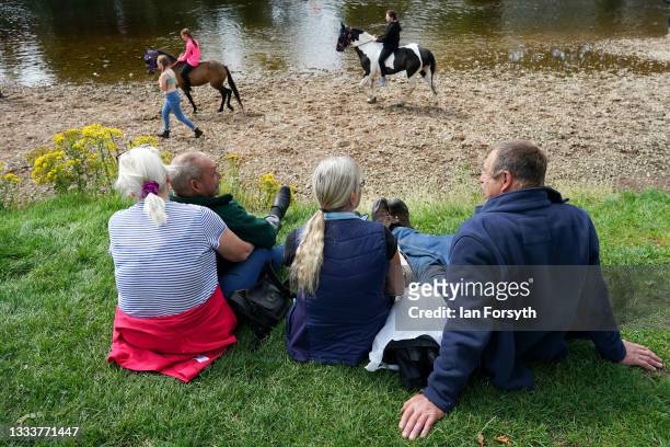 People sit on the river bank as horses are ridden in the River Eden on the first day of the Appleby Horse Fair on August 12, 2021 in Appleby,...