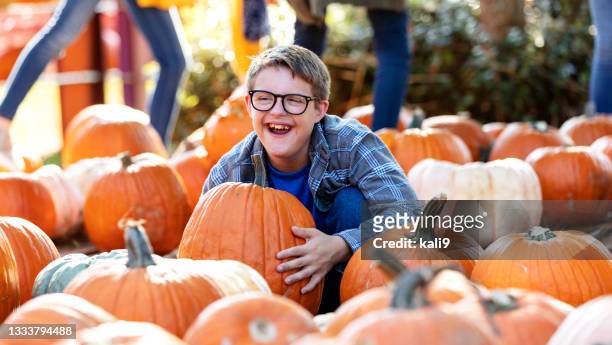 boy with down syndrome having fun in pumpkin patch, smiling - pompoenenveld stockfoto's en -beelden