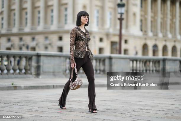 Hélène Guillaumes wears silver large earrings, a silver chain necklace with silver butterfly pendant, a beige / brown / black leopard print pattern...