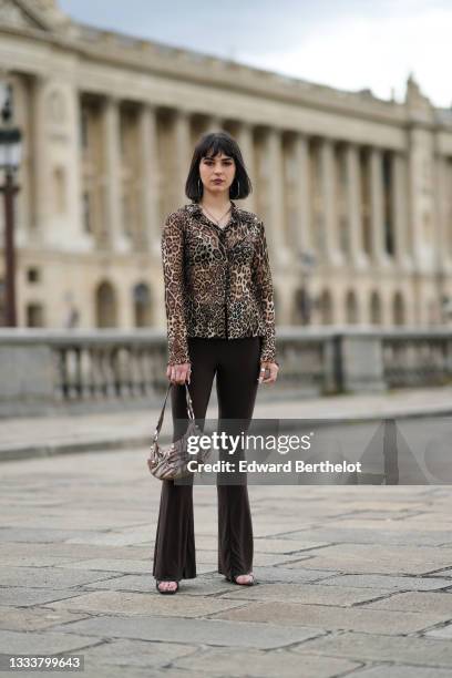 Hélène Guillaumes wears silver large earrings, a silver chain necklace with silver butterfly pendant, a beige / brown / black leopard print pattern...