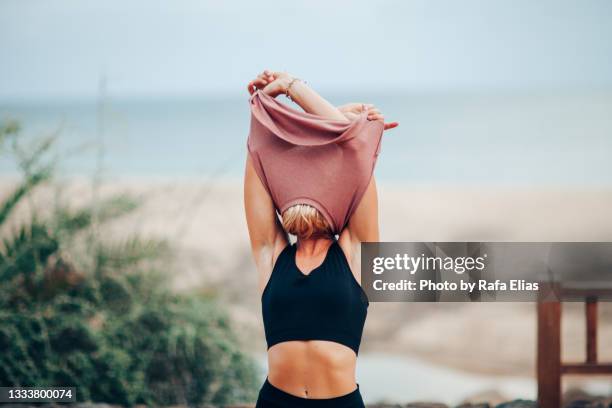 woman taking off t-shirt and showing her shaved armpits - warm up exercise stock-fotos und bilder