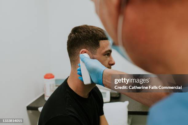 a health care worker inserts an infrared ear thermometer into a male patients ear - ear drum stockfoto's en -beelden